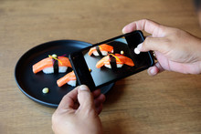 He Is Using A Cellphone, Taking A Picture Of Sushi, Placed In Front Of A Japanese Restaurant.