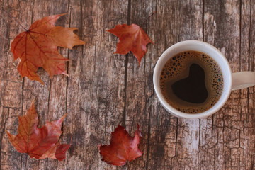 Coffee and red maple leaves on vintage wooden background. Autumn drink concept. October, November, thanksgiving, fall foliage