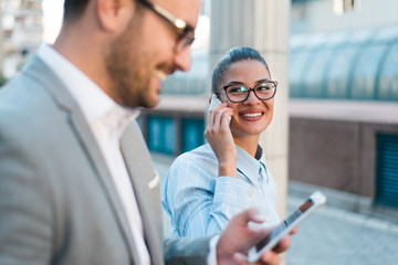 Two young successful happy business people working together, walking in the city, talking on the phone and smiling. 