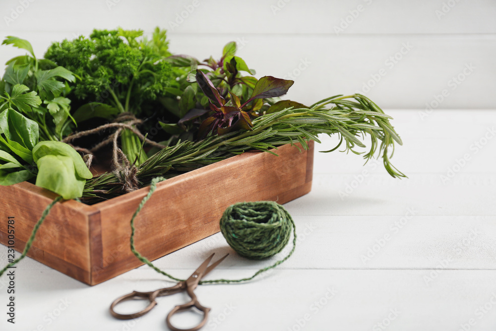 Box with fresh aromatic herbs and scissors on white table