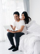 © nuiiko - Happy Asian couple using laptop on bed together at home, lifestyle concept.