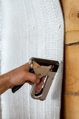 Wall Mural - A man's hand with the help of a construction stapler is attached to a wooden beam with foil insulation for a sauna. Close-up.