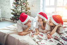 Family In Christmas Santa Hats Lying On Bed.
