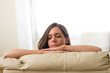 © Gerard - Serious brunette girl leaning on her two arms on a beige sofa looking to the side thoughtfully with her hair behind her ear
