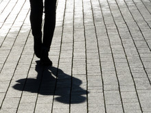 Silhouette Of Person Walking Down The Street. Legs Of Slim Girl, Shadow On Pavement, Concept For Loneliness, Dramatic Stories