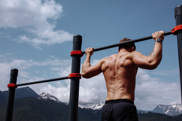 Caucasian male athlete with fit torso and strong hands doing chin ups outdoor. Handsome blonde sportsman pulls up on stadium horizontal bar. Chin up bar exercises.