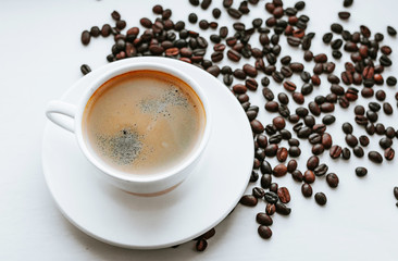 White cup with fresh coffee on saucer close up with grains of coffee on white isolated background