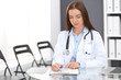 © rogerphoto - Doctor woman at work. Portrait of female physician filling up medical form while sitting at the glass desk at clinic or hospital. Medicine and healthcare concept