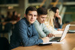 © Aleksandr - Group of college students studying in the school library, a girl and a boy are using a laptop and connecting to internet. Boy look to the camera