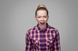 © khosrork - Angry beautiful blonde girl in red, pink checkered shirt, collected bun hairstyle, makeup standing and looking at camera with and screaming. indoor studio shot. isolated on gray background