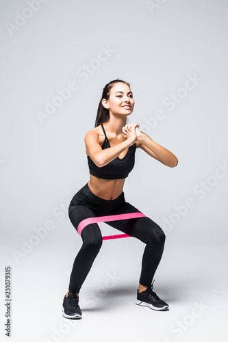 Cuadros en Lienzo Young fitness woman doing squats with fitness loop band isolated on white backgr