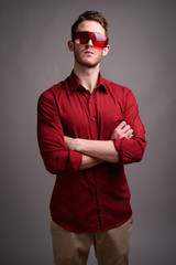 Young handsome businessman wearing red shirt against gray backgr