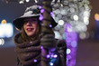 © qunica.com - Young girl standing in front of christmas tree lights at night with snowflakes falling, snowing