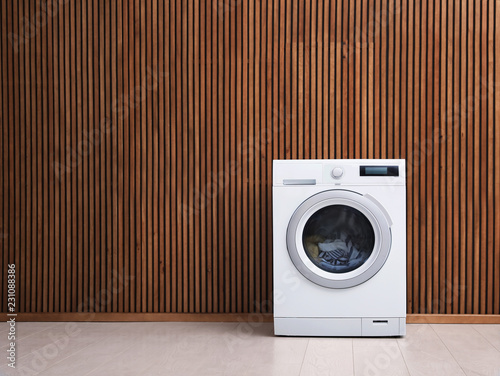 Fotografie, Obraz Washing machine with laundry near wooden wall. Space for text