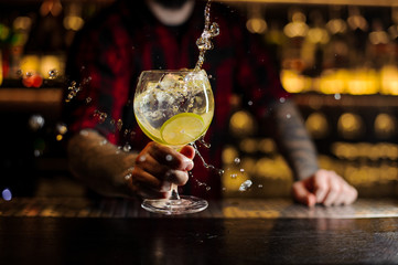 Bartender making splash of a delicious Gin Tonic cocktail with lime slices