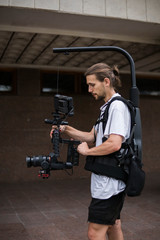 Professional videographer holding camera on 3-axis gimbal which mounted on easy rig. Videographer using steadicam. Pro equipment helps to make high quality video without shaking.