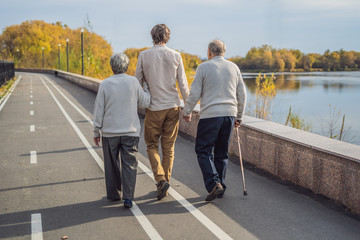 An elderly couple walks in the park with a male assistant or adult grandson. Caring for the elderly, volunteering