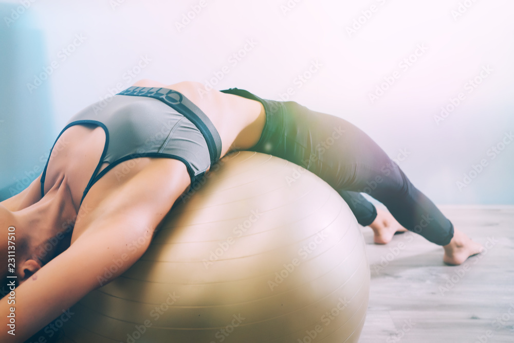 Woman working out with exercise ball in gym. Pilates woman doing exercises in the gym workout room with fitness ball. Fitness woman doing exercises for muscle press with abs swiss ball. - obrazy, fototapety, plakaty 