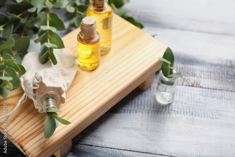 Wooden board with bottles of eucalyptus essential oil on table