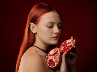 Wall Mural - portrait of a young girl with red hair and pomegranate fruit in hands on red background