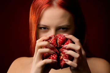 Wall Mural - portrait of a young girl with red hair and pomegranate fruit covering her face on a red background