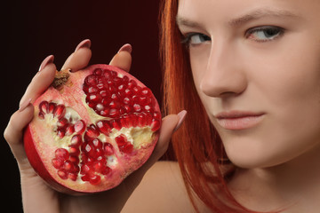 Wall Mural - portrait of a young girl with red hair and pomegranate fruit in hands on red background