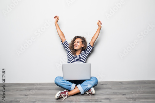 Cuadros en Lienzo Portrait of happy young mixed races curly woman sitting on floor with laptop and