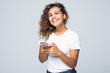 © F8  \ Suport Ukraine - America latin mixed race woman with curly hair holding mobile phone and smiling on camera isolated over white background