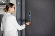 © rh2010 - Young business woman in white suit touching the intercom with keychain opening the door of residential modern building