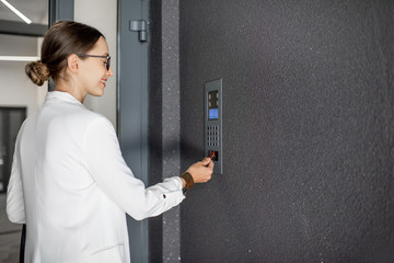 Young business woman in white suit touching the intercom with keychain opening the door of residential modern building