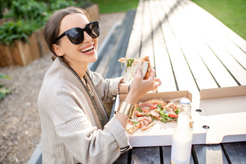 Wall Mural - Young woman having a snack with pizza sitting outdoors at the modern public park