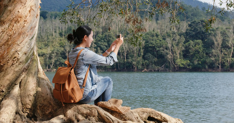 Wall Mural - Woman take photo on cellphone and sit on the old tree root in forest