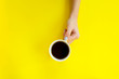  Woman hand holding coffee cup on yellow background.