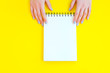 Woman hand holding notebook on yellow background.