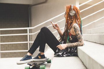 young girl with tattoo and dreadlocks listening to music while sitting on the steps