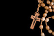 A brown rosary lying on a black background