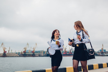 Two college women students of Marine academy walking by sea wearing uniform. Friends walking and pointing into distance