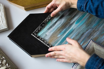 Picture framing. Choosing decorative frame for a painting. Woman's hands and samples of frames.