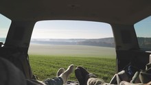 Personal perspective of couple lying in car's trunk, mountain landscape and admiring sunrise . Lovers alking and drinking hot coffee against backdrop of forest panorama in fog . View from inside 4k