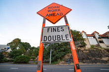 Road Side Orange Sign With "Road Work Ahead" On It Followed By "fines Double"