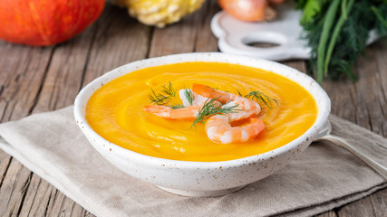 Wall Mural - Delicious yellow pumpkin cream soup with shrimp on dark gray old rustic wooden table, side view, long format banner