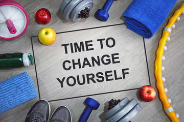 Time to change yourself. Fitness motivational quotes. Sport theme. Healthy and active lifestyle concept. Sneakers, hoop, wheel, towel, dumbbells, apples and a workout mat on grey wooden background.