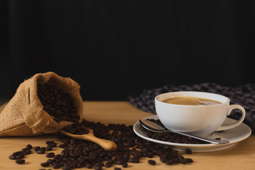 coffee in cup and coffee beans in a sack on wood table with black background