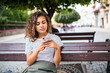 © F8  \ Suport Ukraine - Young beauty curly latin woman typing on the phone while sitting on the bench on the street
