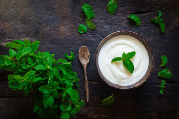 Greek yogurt or sour cream with a mint leaf  in a wooden bowl on dark table top view. Healthy food nutrition.