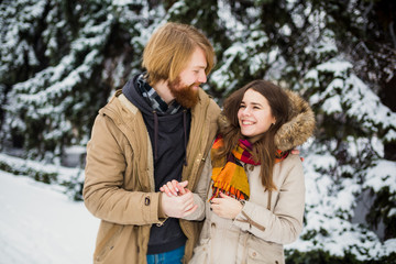  Young Caucasian boy and girl in love heterosexual couple have a date outdoors in a winter park on the background of a snowy conifer standing in an embrace. Man hugging woman valentines day