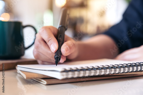 Fotomural Closeup image of a woman's hand writing on blank notebook with coffee cup on tab