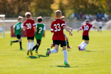 Boys kicking football on the sports field. An action sport picture of a group of kids playing soccer football tournament game under the sunset.