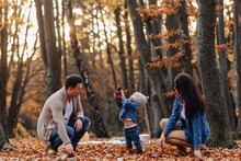 Happy Family With Little Cute Child In Park On Yellow Leaf With Big Pumpkin In Autumn