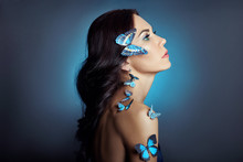 Beautiful Mysterious Woman With Butterflies Blue Color On Her Face, Brunette And Paper Artificial Blue Butterflies On The Girls Body. Bright Green Eyes, Long Black Curly Hair